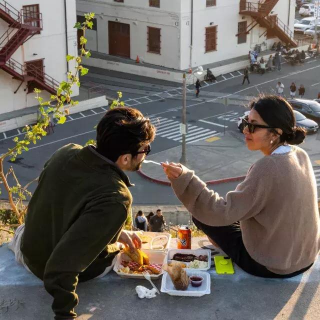 Una pareja cena al aire libre en el Fort Mason Center en San Francisco. La mujer le da a su compañero un poco de comida.